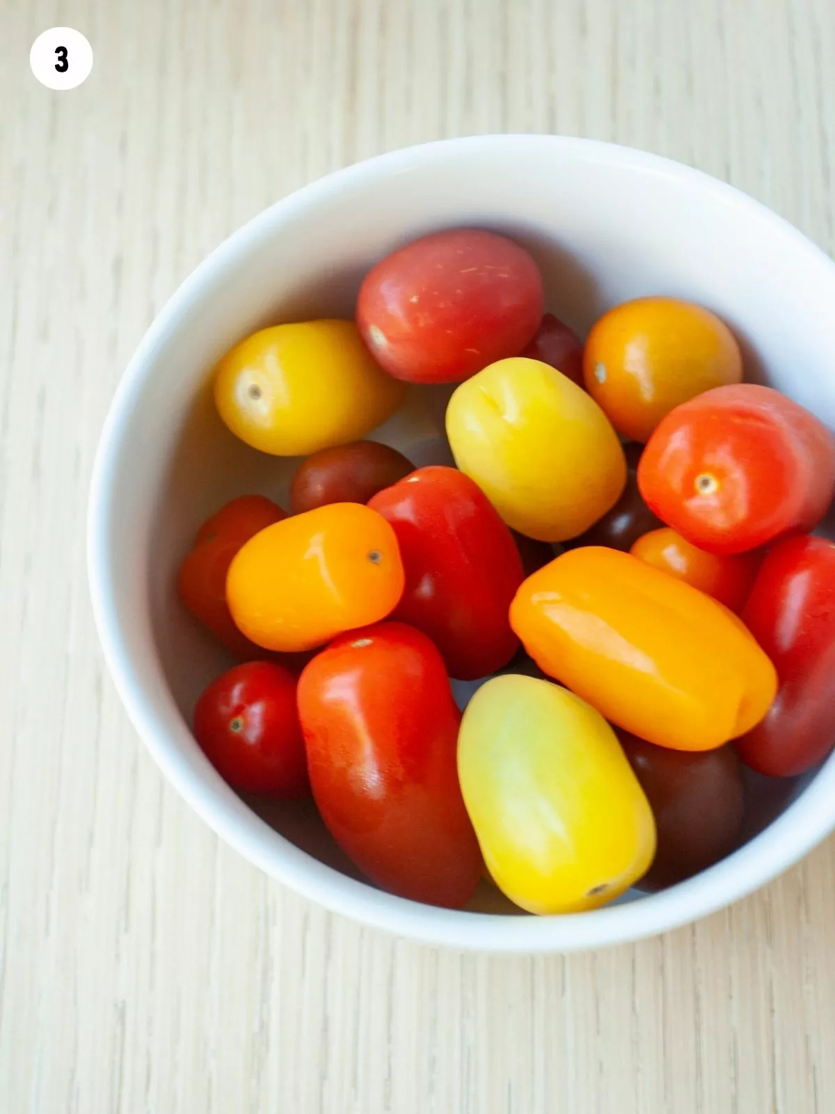 multi colored tomatoes in white bowl.