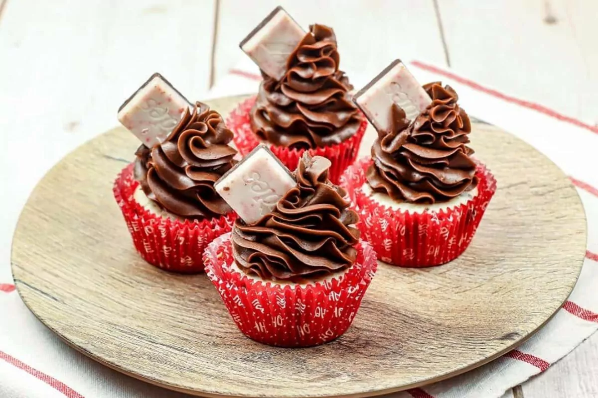 four cupcakes with chocolate frosting and a piece of chocolate bar toppings in a wooden plate