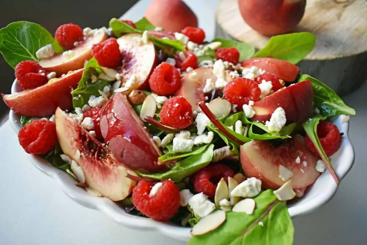 A bed of greens topped with berries, peaches, almonds and cheese.