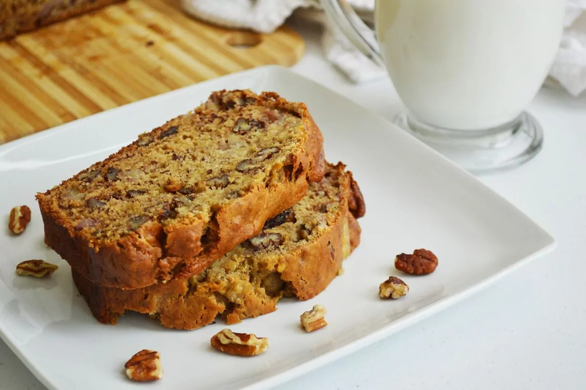 2 slices banana bread on white plate with pecan pieces scattered around.