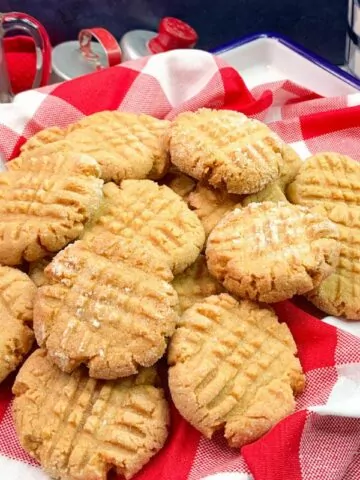 Peanut butter cookies piled on top of a red plaid napkin.