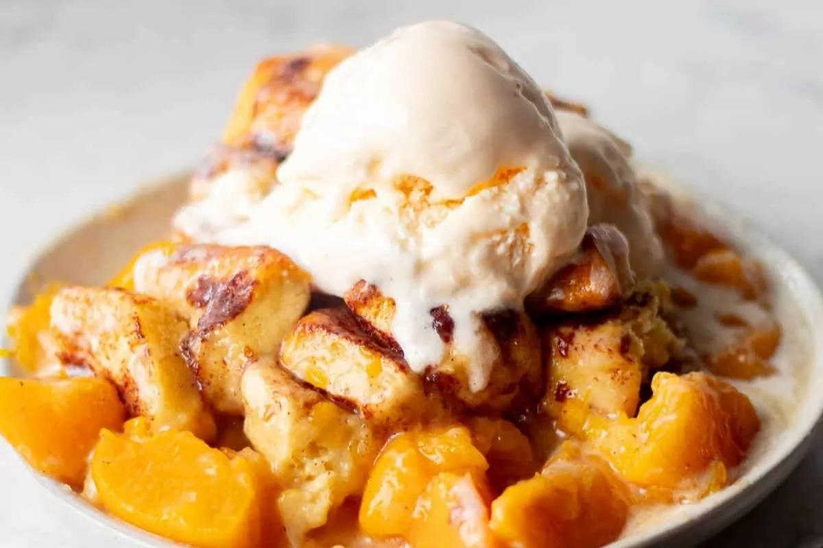 A plate of peaches topped with cinnamon rolls and ice cream.