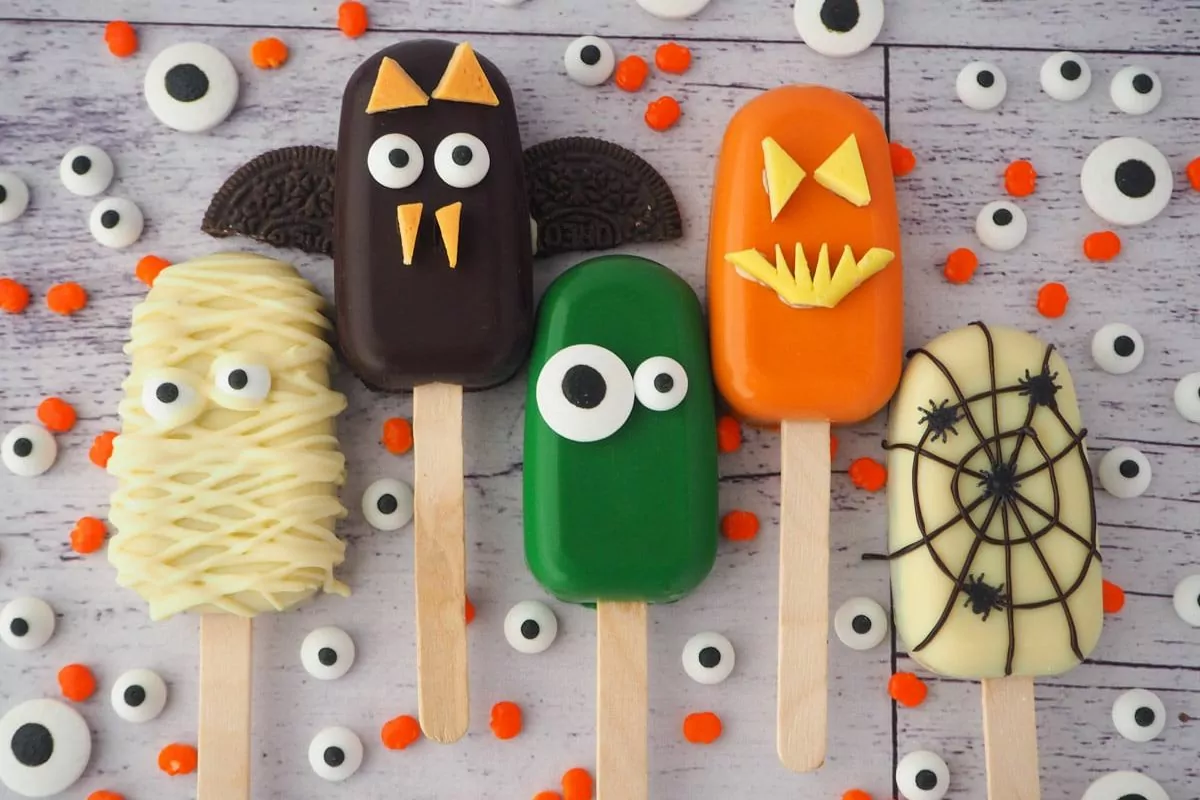 Cakesicles decorated like pumpkins, monsters, spider webs, mummies and bats for Halloween.