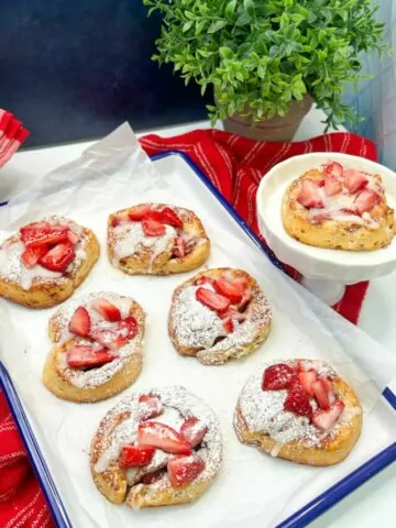 cinnamon rolls with powdered sugar and strawberries on white tray.