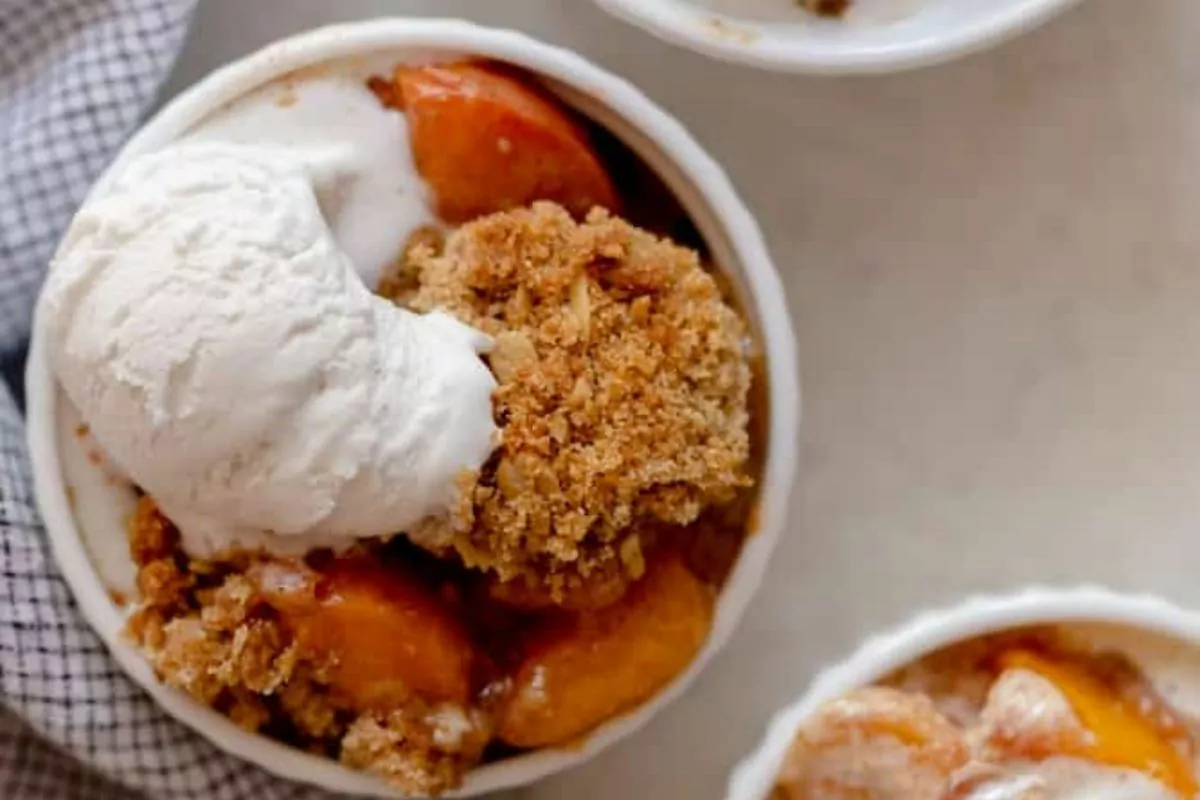 A small bowl of peach crisp with oatmeal topping and a scoop of vanilla ice cream.