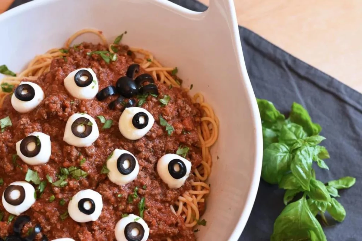 a pot of spaghetti with cheesy eyes scattered over the top.