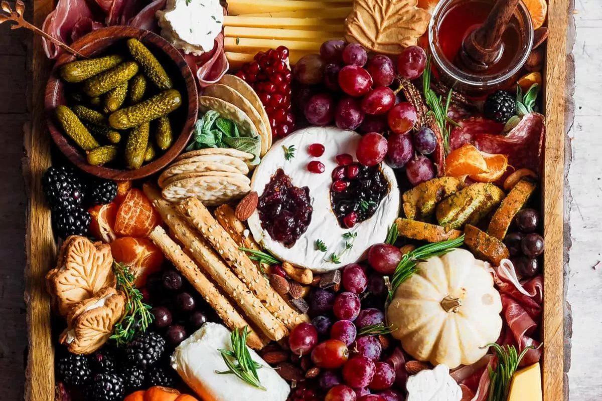 a charcuterie board has meat, cheese, veggies, fruits, nuts and an assortment of crackers.