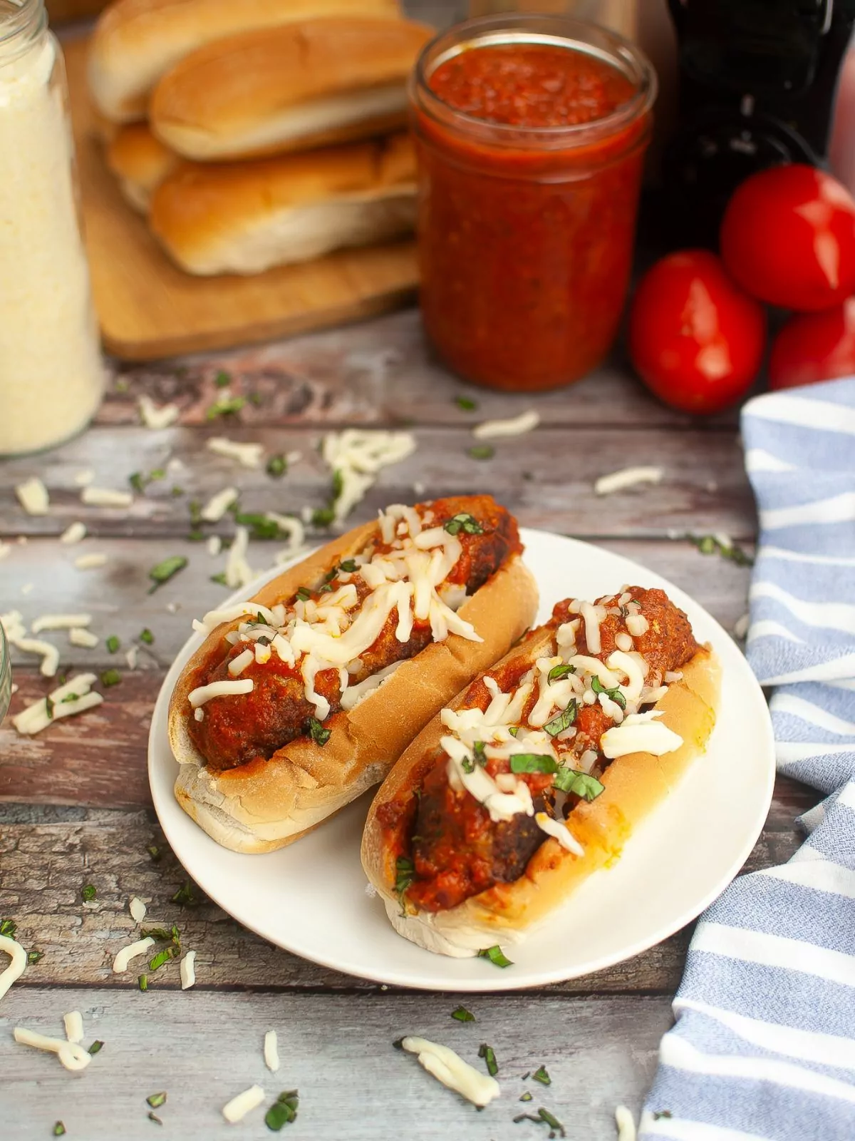 two meatball subs served on a white plate with ingredients in the background