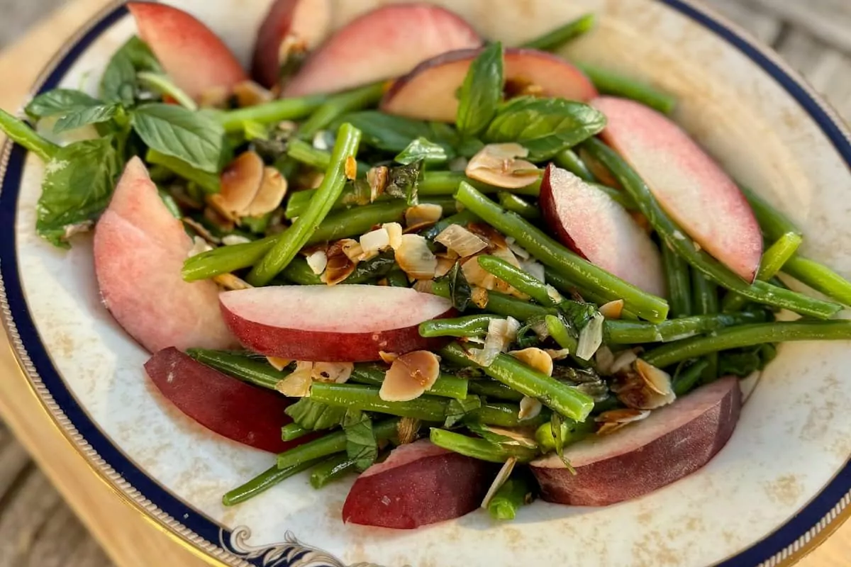 A serving dish of french style green beans with nuts and peach slices.