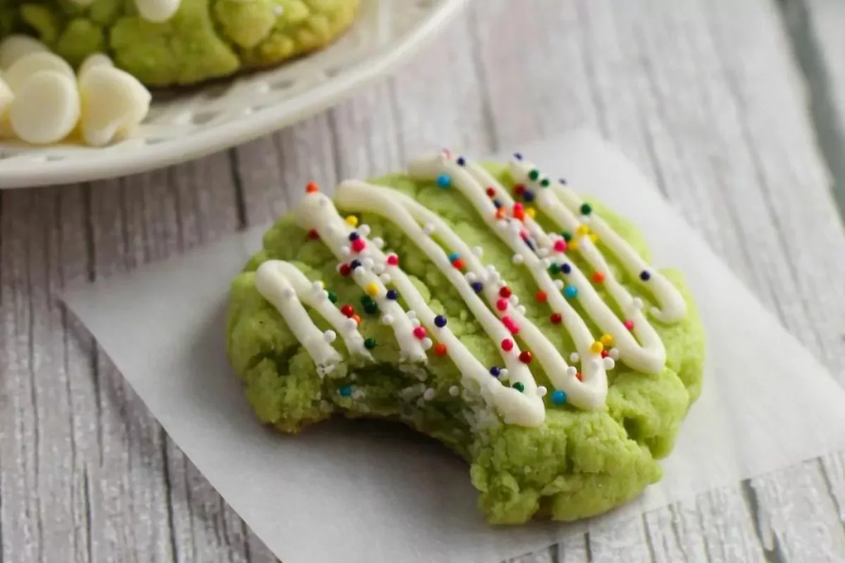 A green cookie with sprinkles and a little frosting.