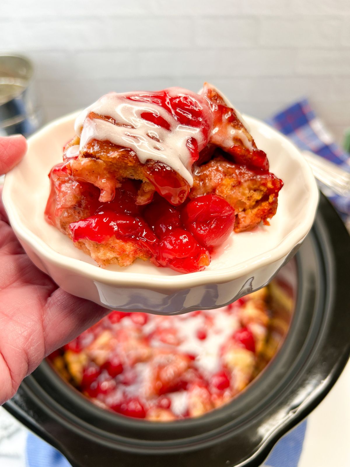 hand holding the plate of cherry cinnamon rolls with the slow cooker in the background