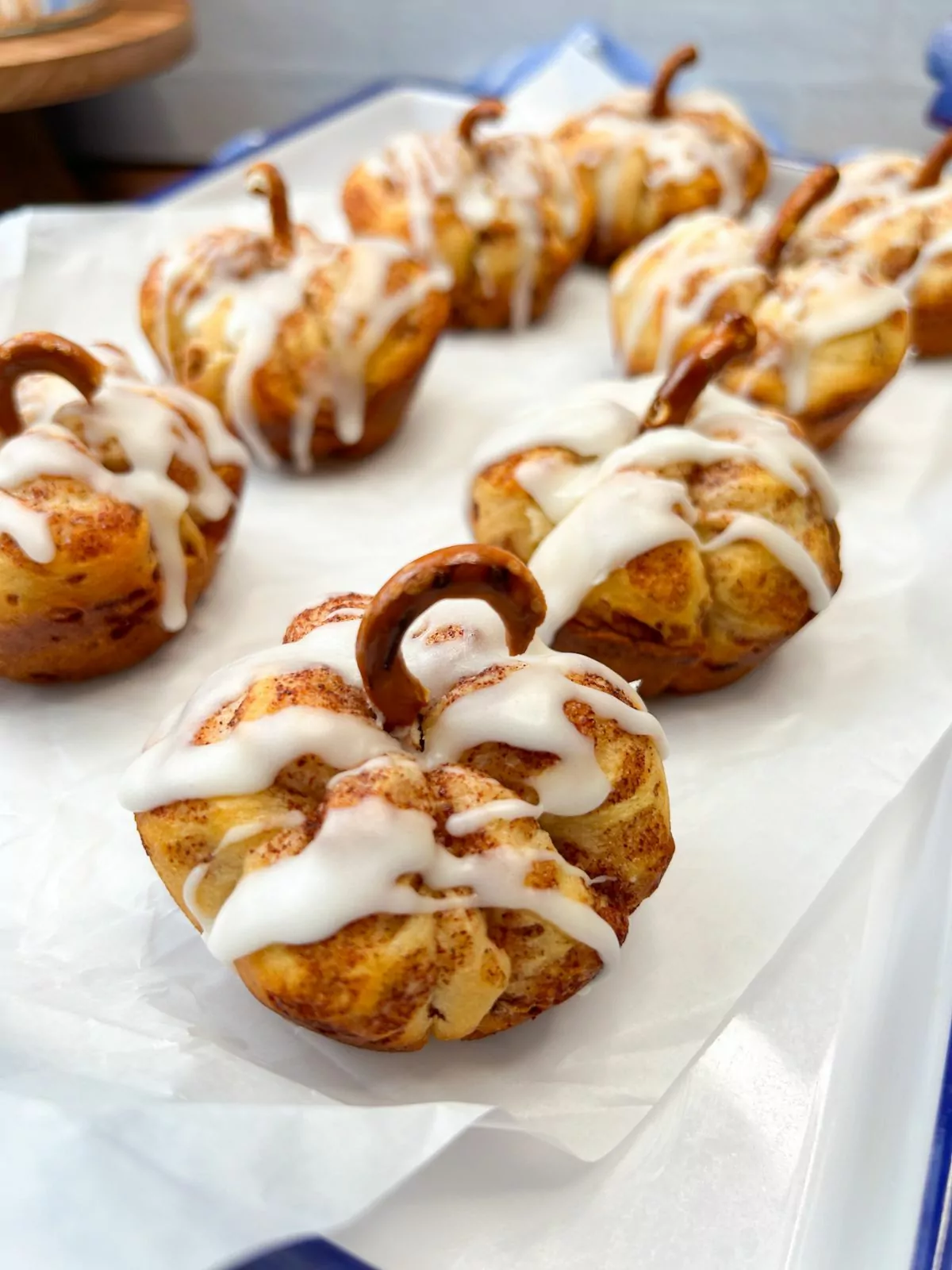 white tray with parchment paper and pumpkin rolls with pretzel stems.