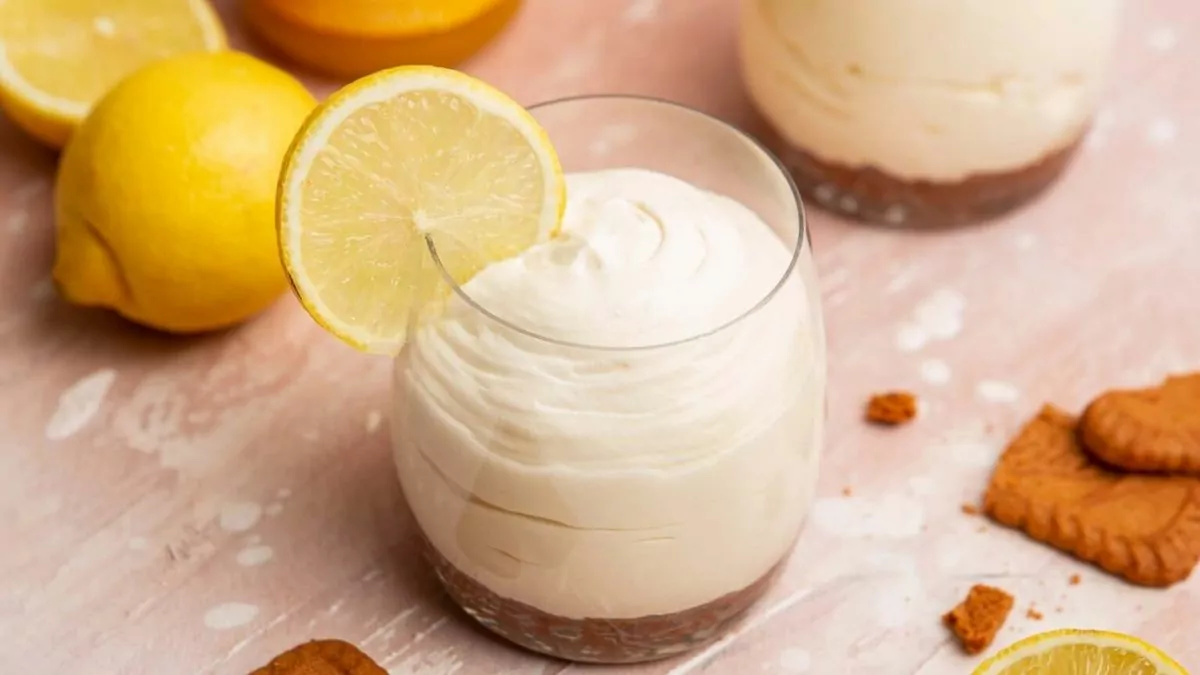 A jar of lemon mousse with cookie crumb crust and a lemon wedge.