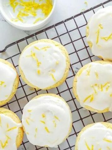 A cooling rack with lemon cookies, topped with glaze and lemon zest.