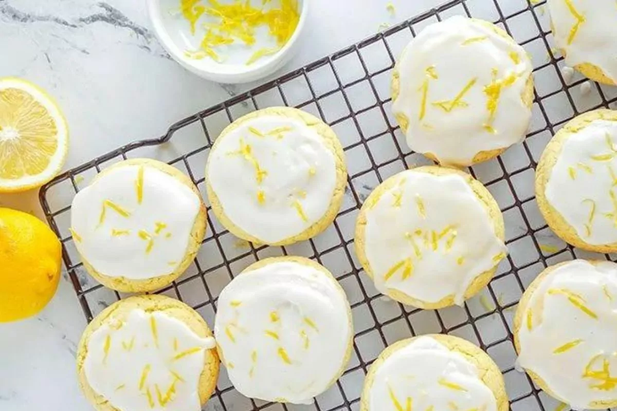 A cooling rack with lemon cookies, topped with glaze and lemon zest.