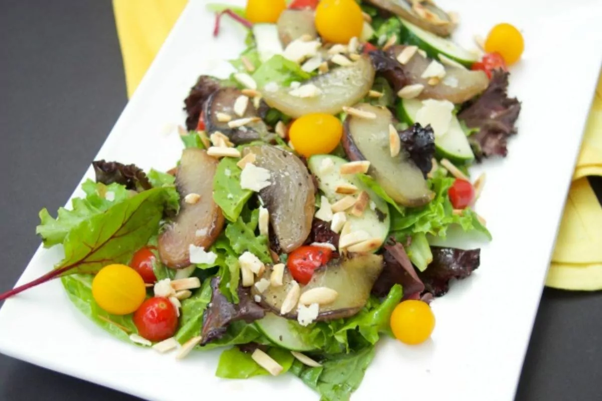 A salad of greens topped with maple roasted white peaches and tomatoes.