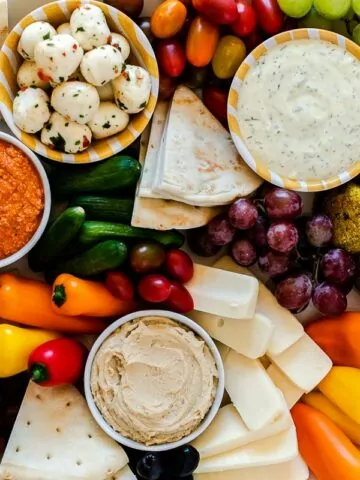 a plate with fruits vegetable cheese and dips