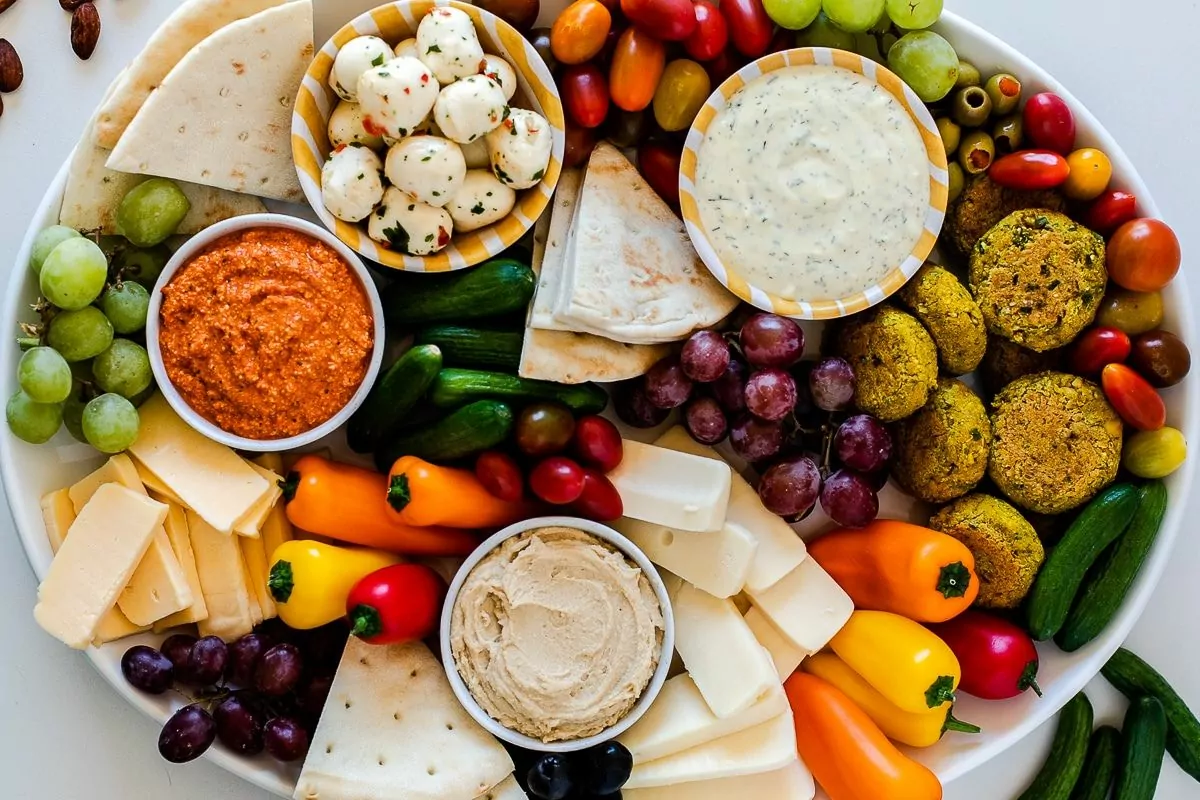 a plate with fruits vegetable cheese and dips