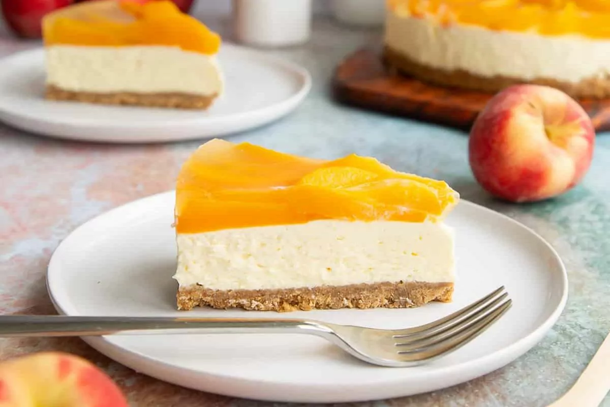 A slice of cheesecake topped with peaches on a plate.