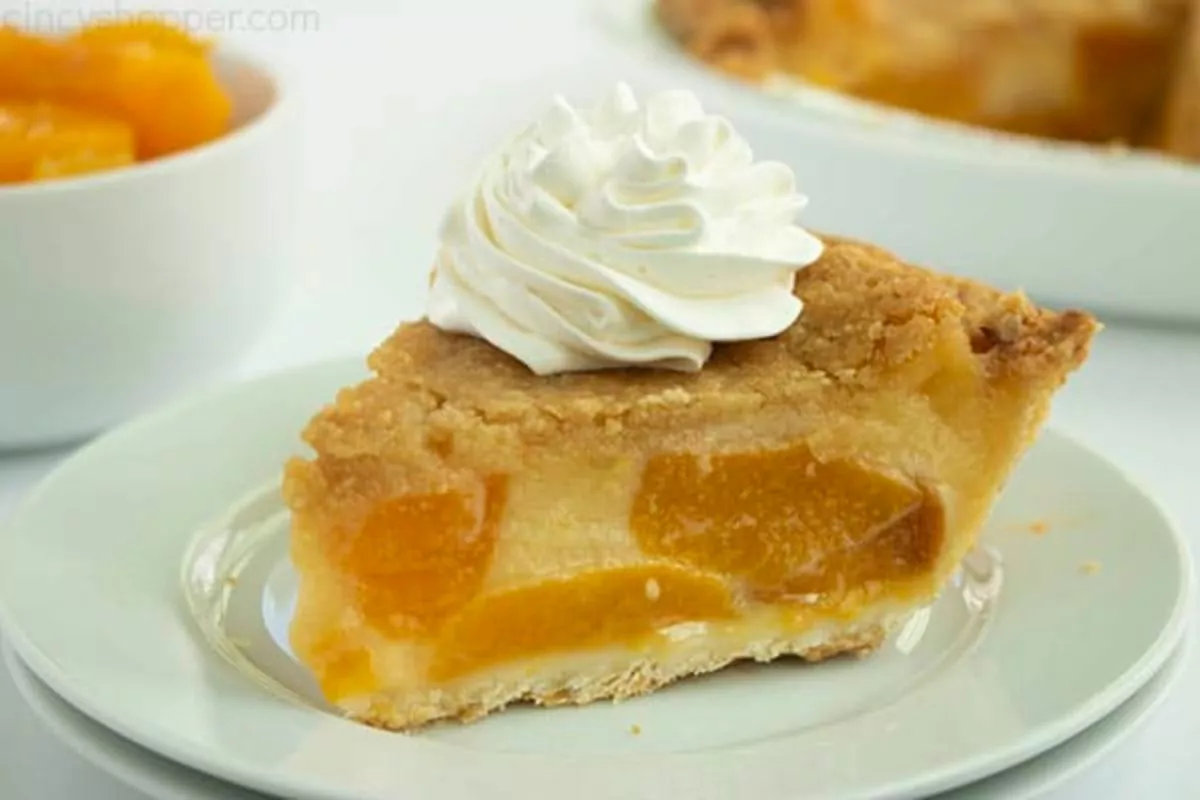 A slice of peach custard pie on a plate with whipped cream.