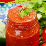 A clear mason jar filled with chunky, vibrant red salsa. Small pieces of tomato, onion, and pepper are visible throughout.
