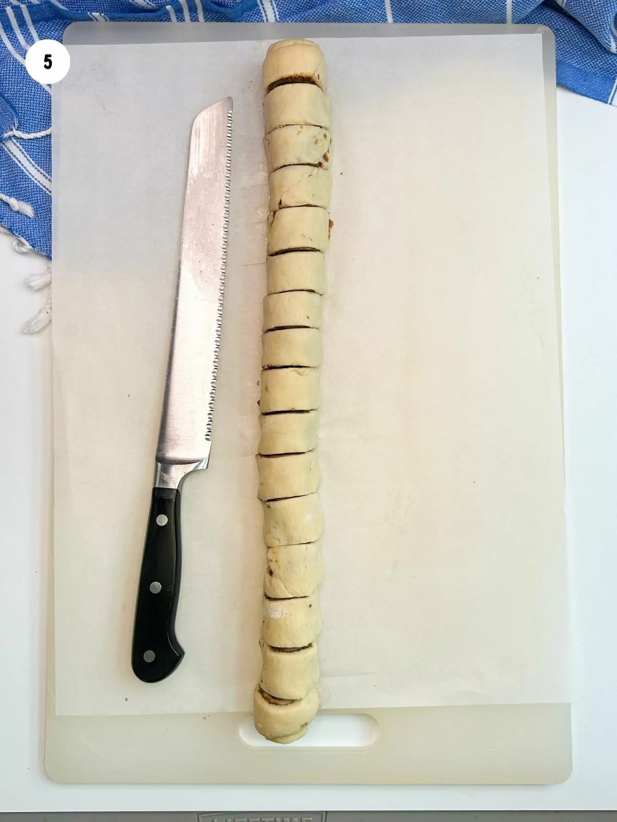 long cylinder of dough sliced on cutting board with serrated knife.