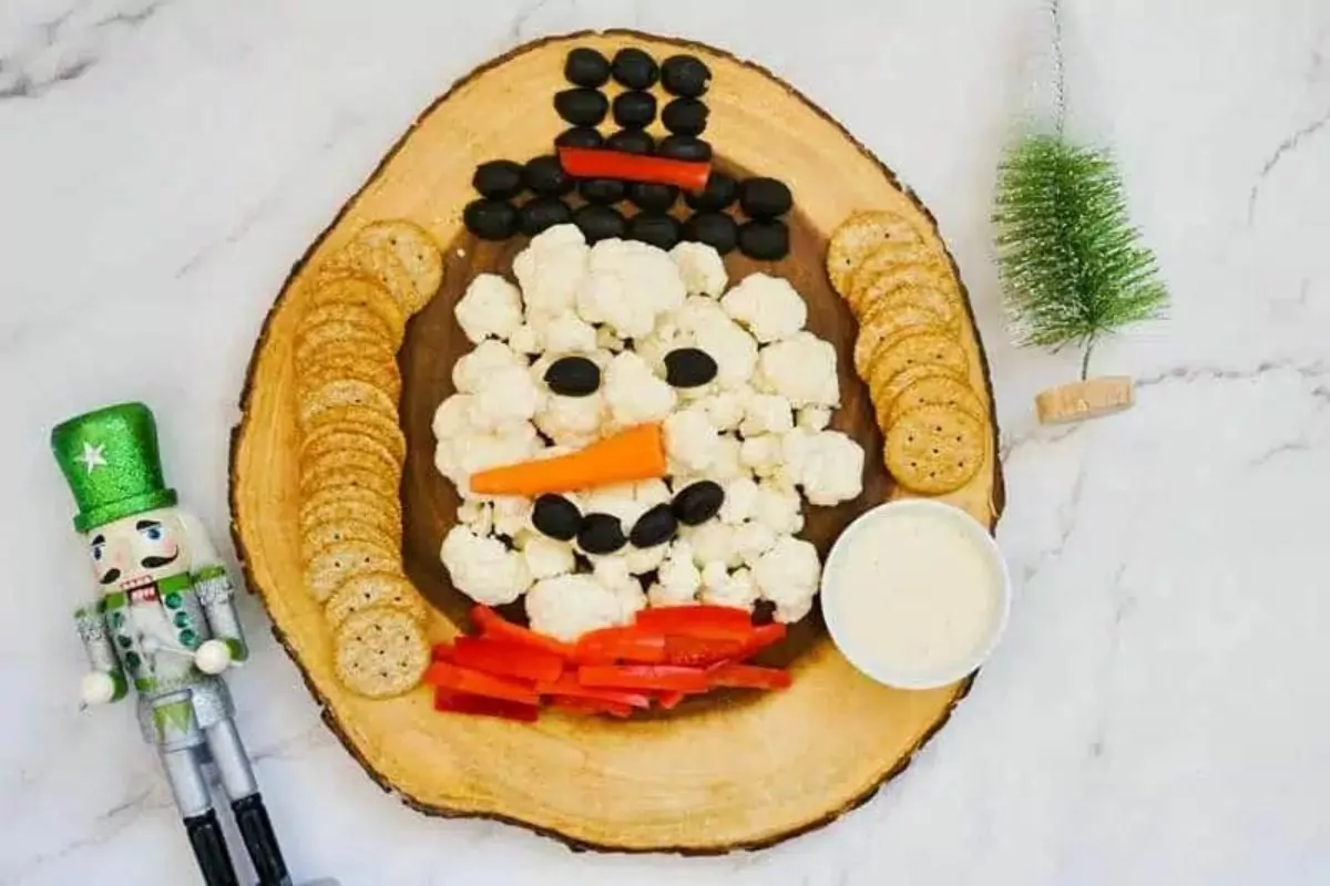 a snowman tray with cauliflower black olives red pepper carrot dipping sauce and crackers