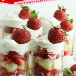 mason jar with cake, strawberries and whipped cream layered with whole strawberries scattered around.