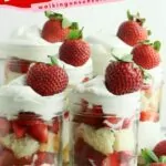 mason jar with cake, strawberries and whipped cream layered with whole strawberries scattered around.