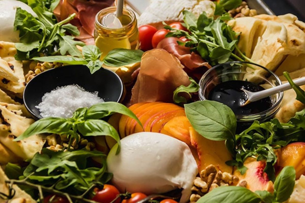 a board that has meat, cheese, fruit, nuts, veggies and crackers