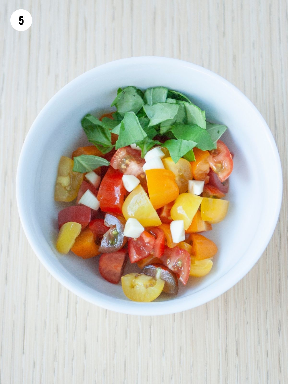 tomatoes with mozzarella cheese and basil leaves in white bowl.