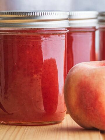 Jars of peach jam with a vanilla bean nearby.