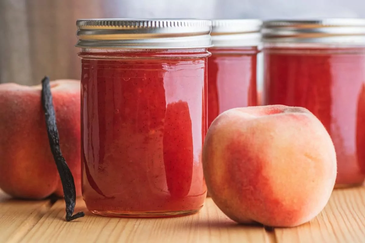 Jars of peach jam with a vanilla bean nearby.