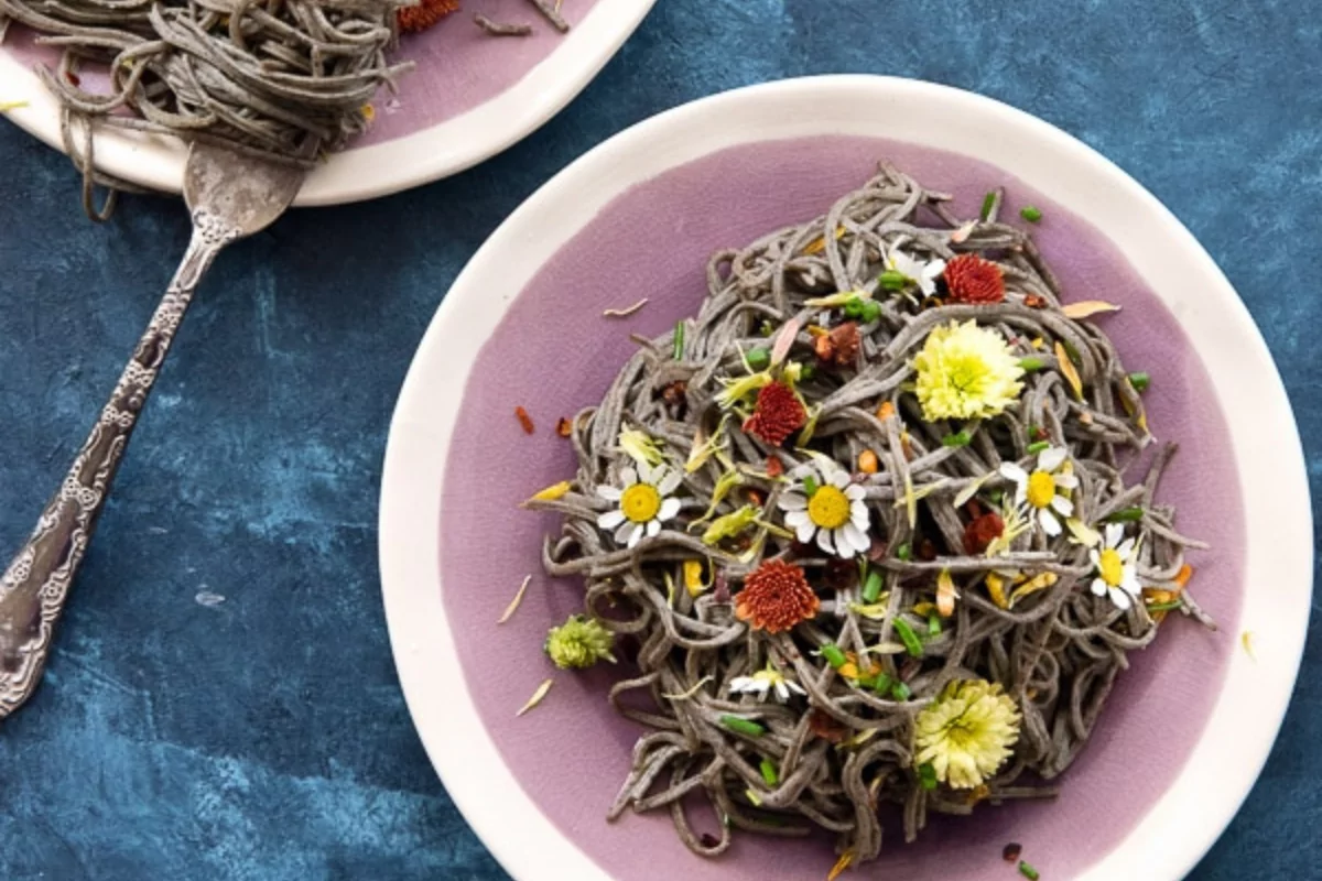 a bowl of pasta with edible flowers and brown butter pasta.