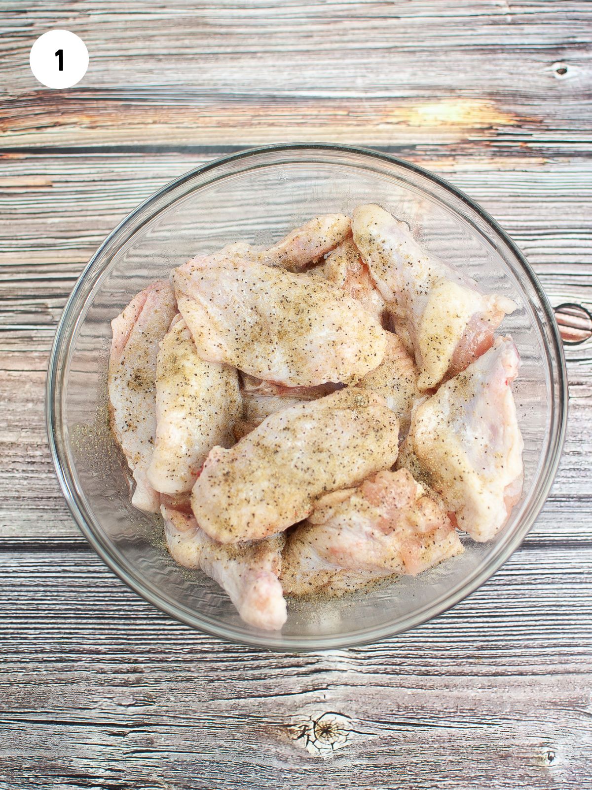 chicken wings in a mixing bowl tossed with oil and seasoning