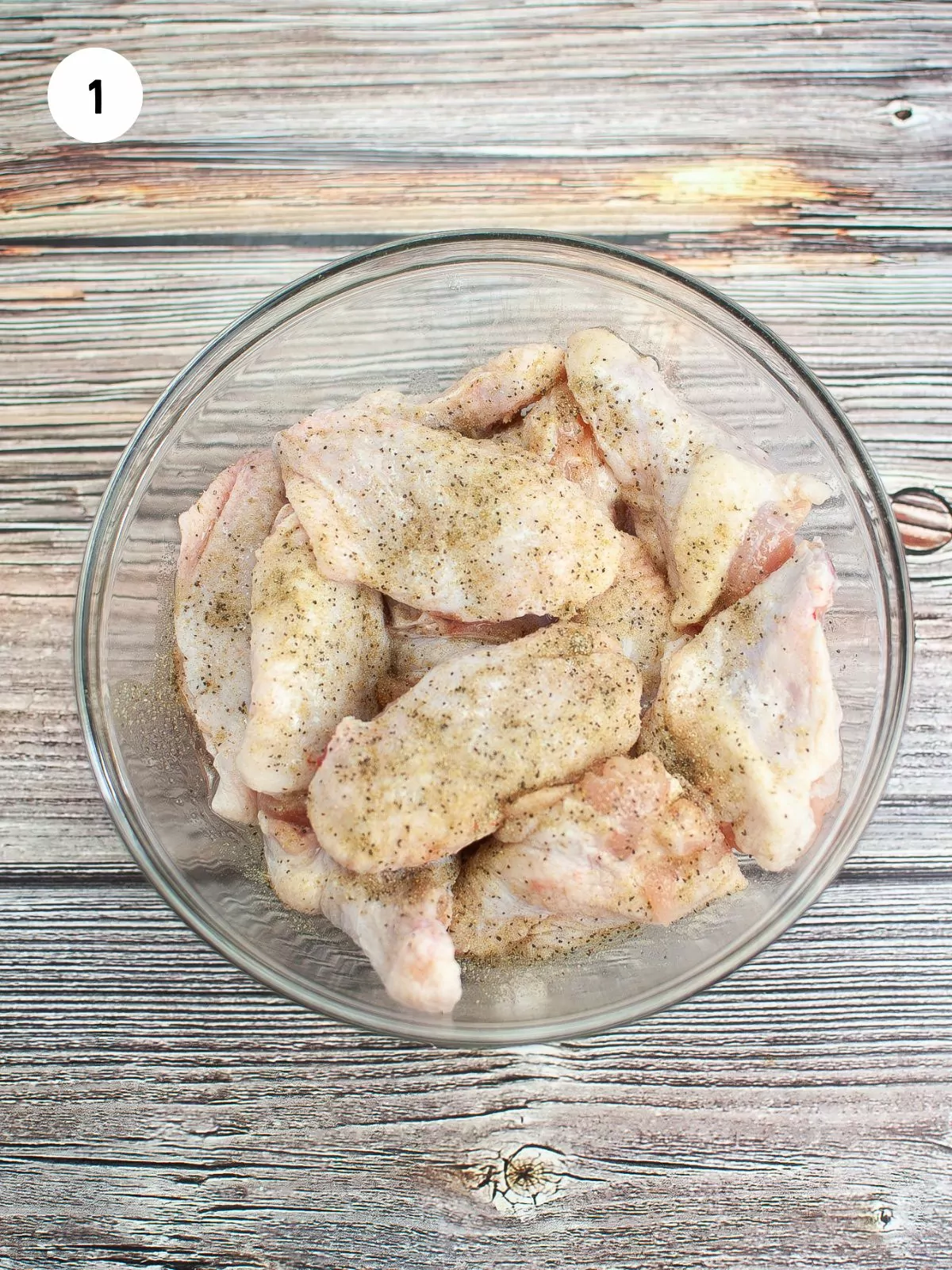 chicken wings in a mixing bowl tossed with oil and seasoning