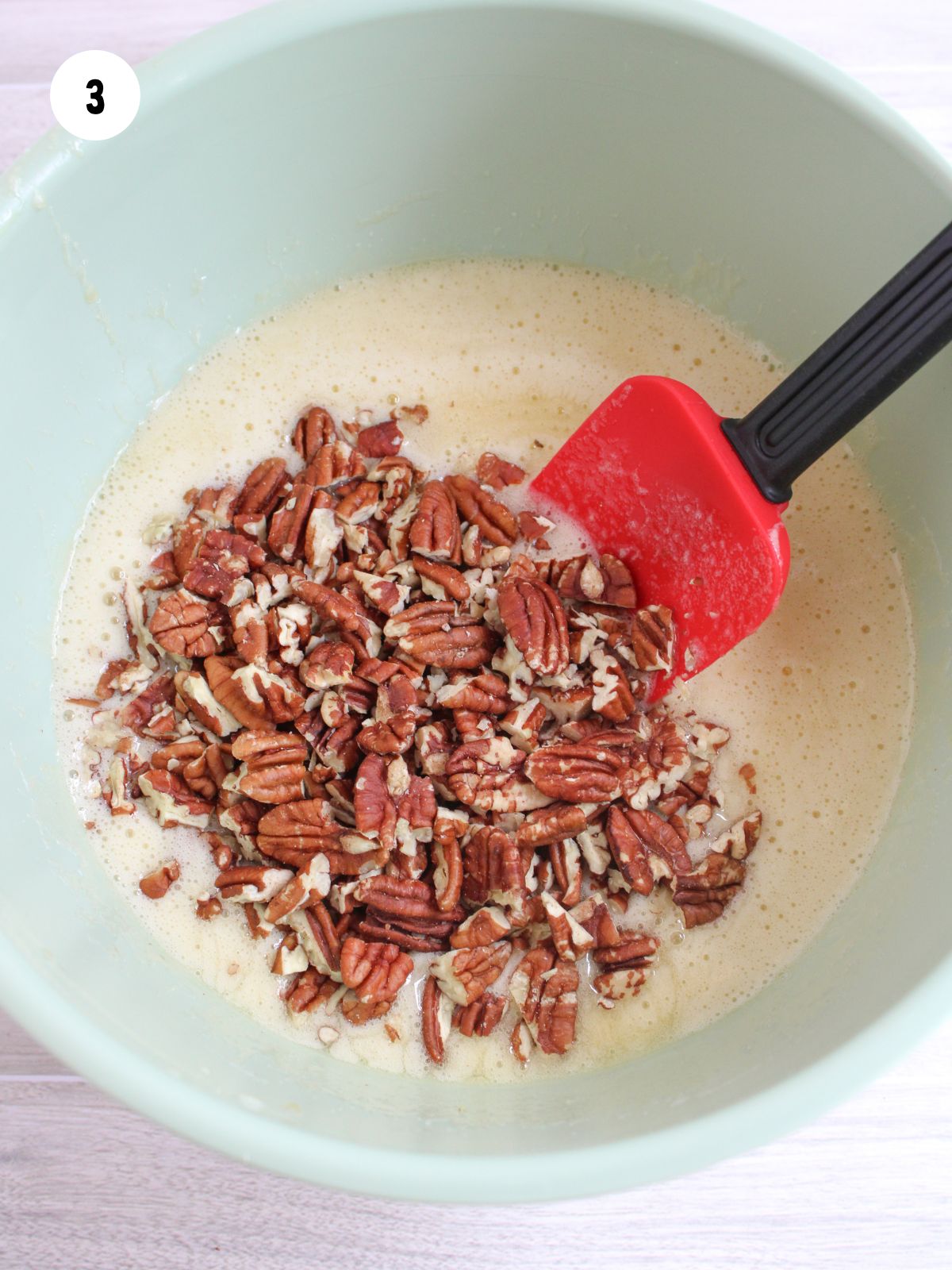 Pecans added to the mixing bowl with a rubber spatula about to stir them in