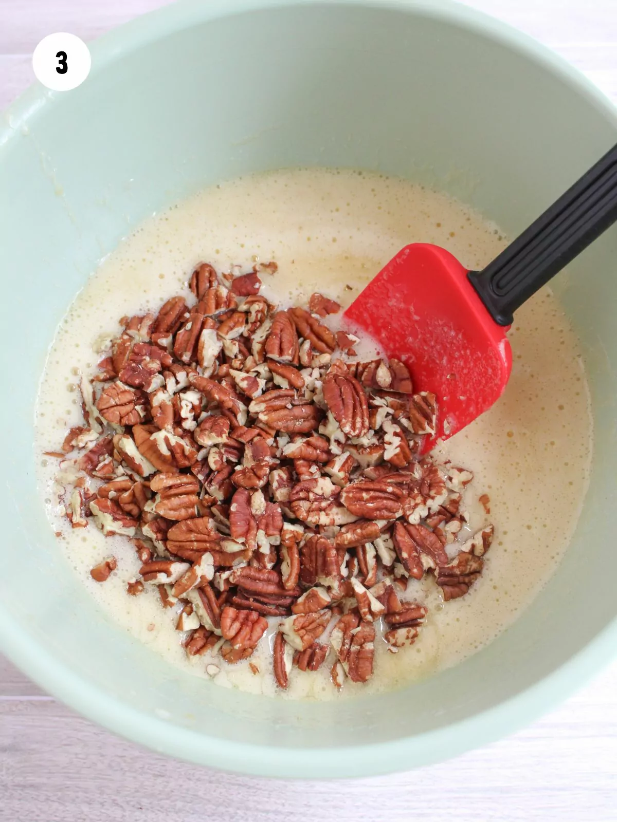 Pecans added to the mixing bowl with a rubber spatula about to stir them in