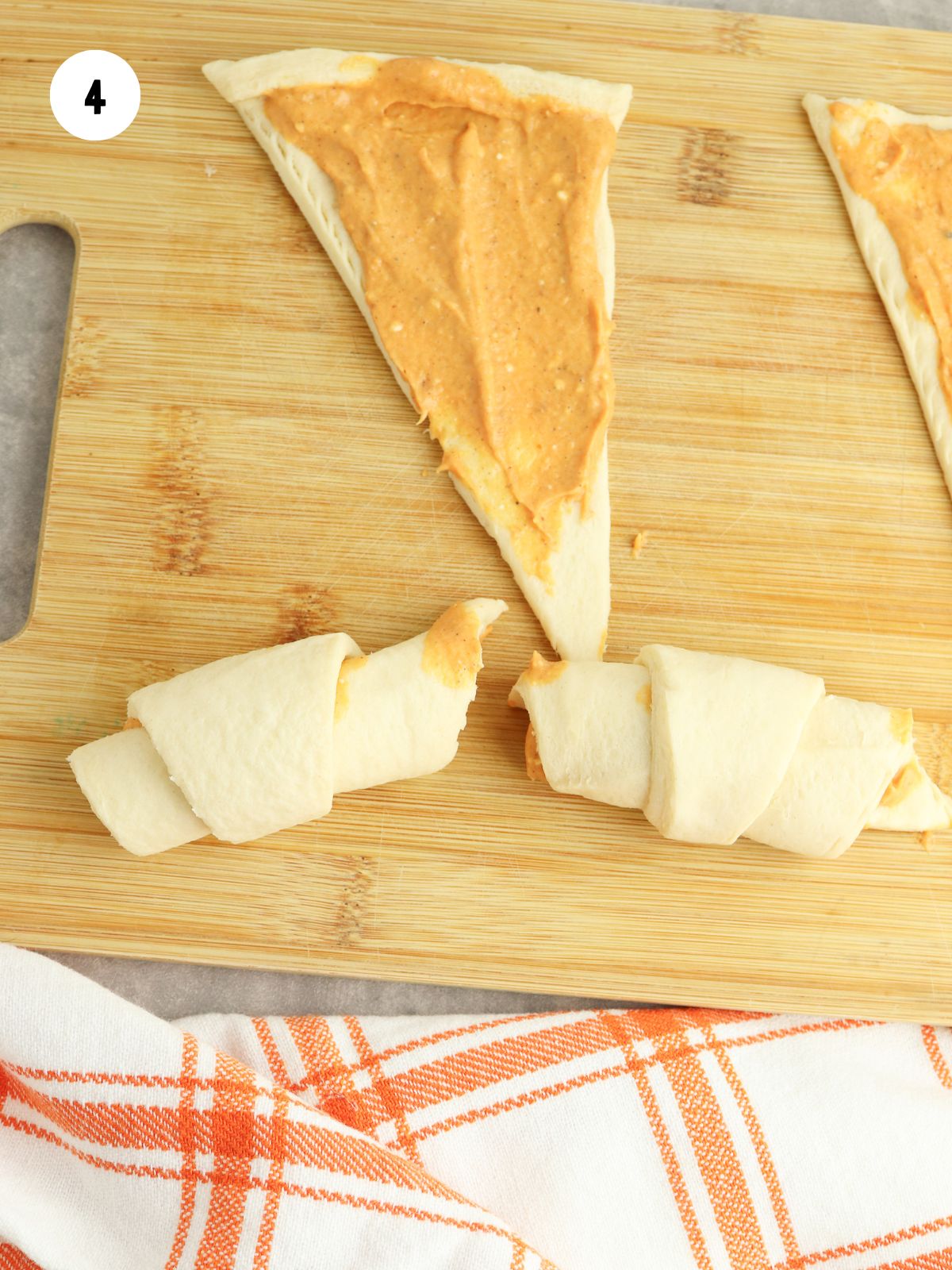 Triangles of dough with pumpkin filling being rolled into crescents