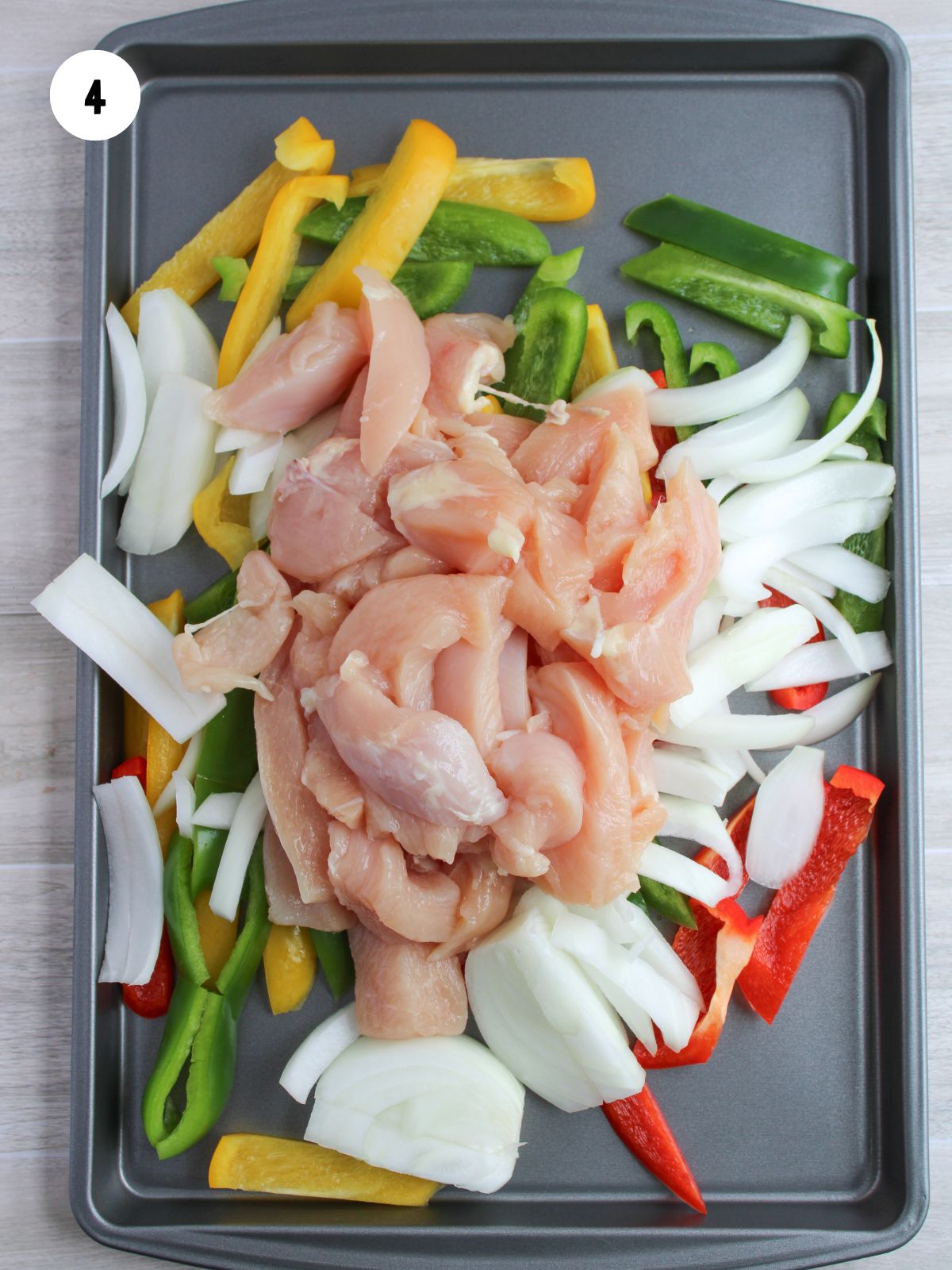 chicken breast strips added on top of the veggies on a sheet pan