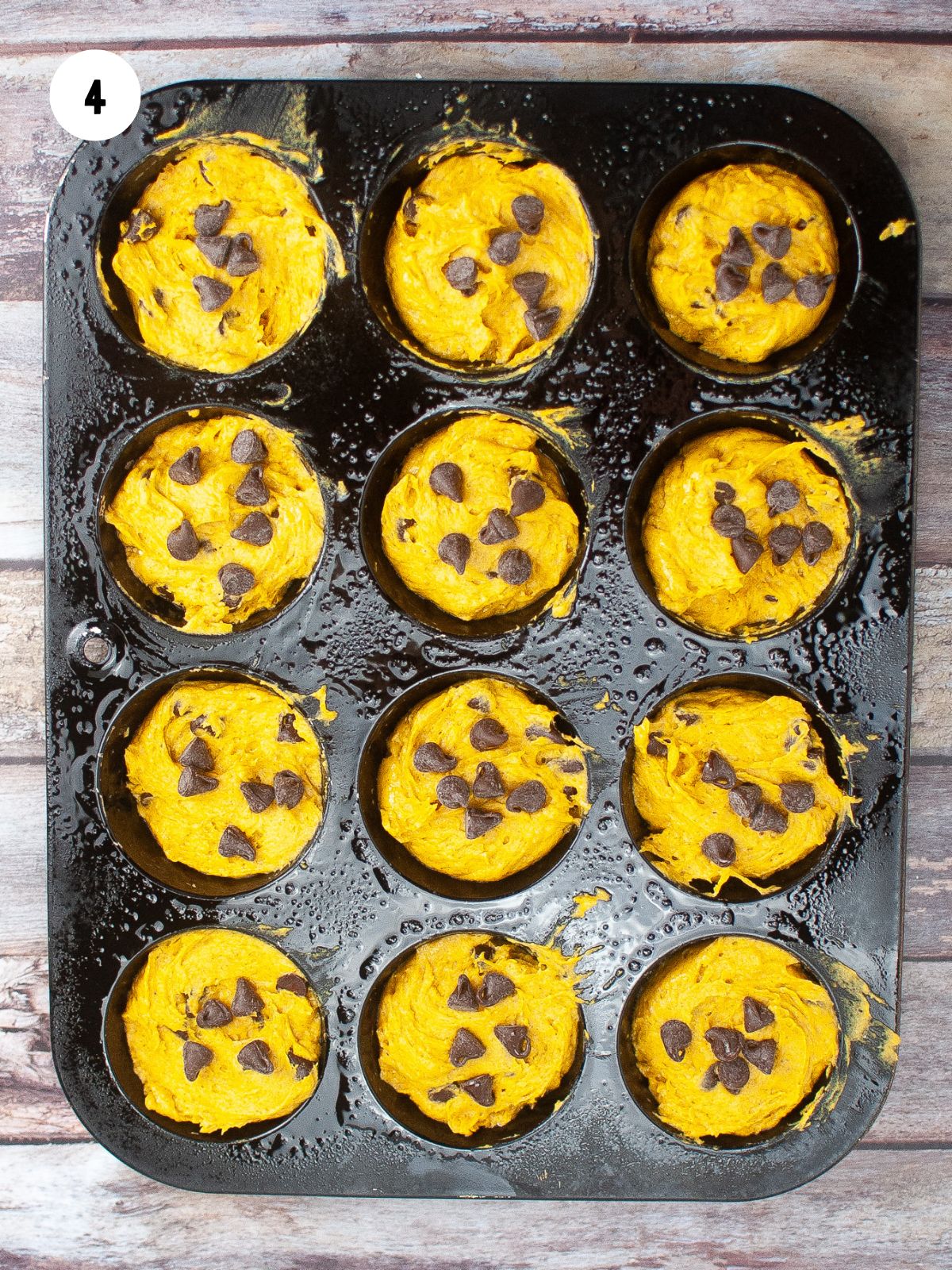 muffin pan filled with pumpkin muffin batter with extra chocolate chips on top of each