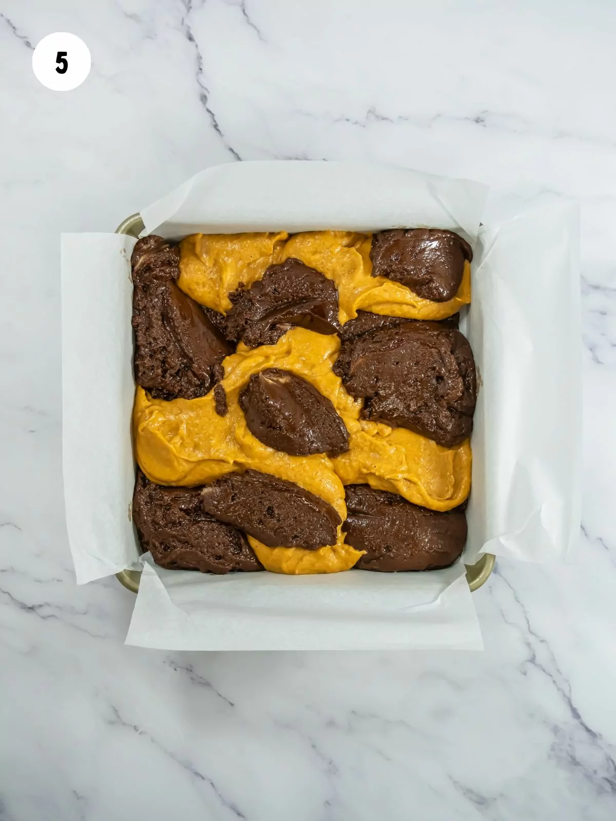 chocolate brownie and pumpkin brownie batter mixed in a square baking pan lined with parchment paper