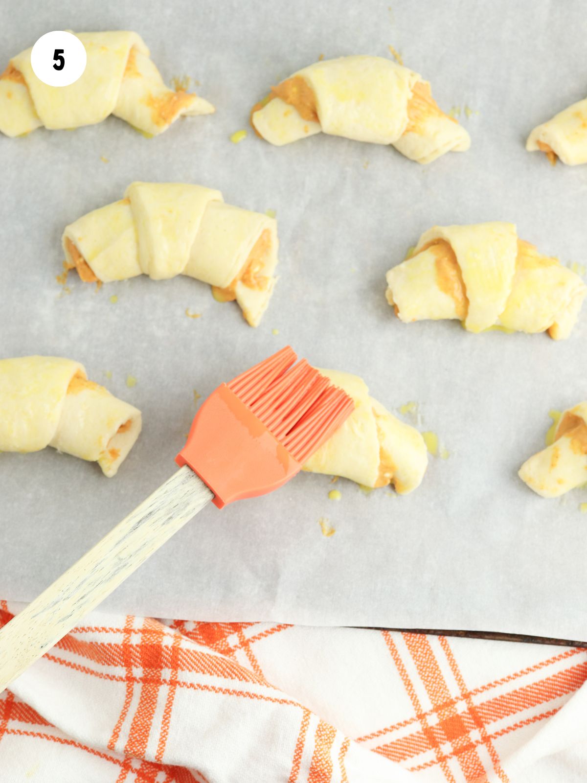 pastry brush brushing egg wash onto the crescents