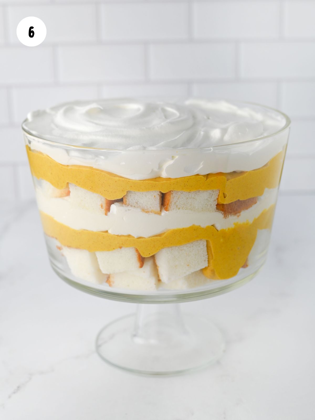 two layers of cake, pumpkin cream cheese, and cool whip in a trifle bowl