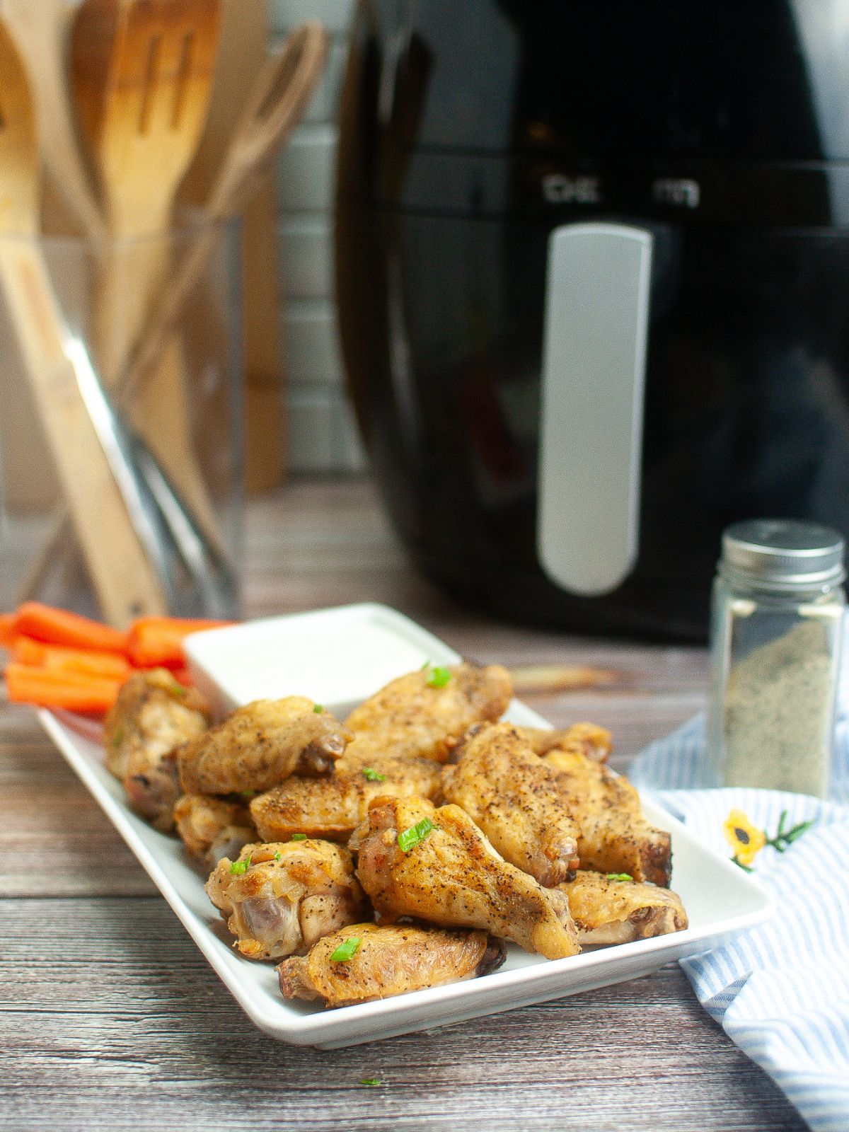 Air Fryer Chicken Wings served with carrot sticks and ranch dressing. Air fryer is in the background