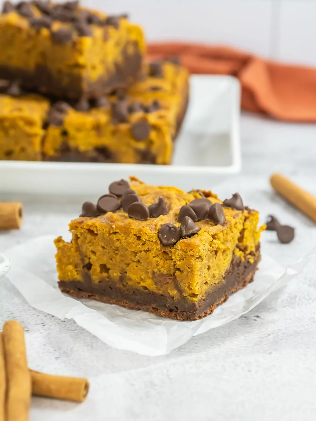 pumpkin brownie on a square of parchment paper with the rest of the brownies on a platter in a background