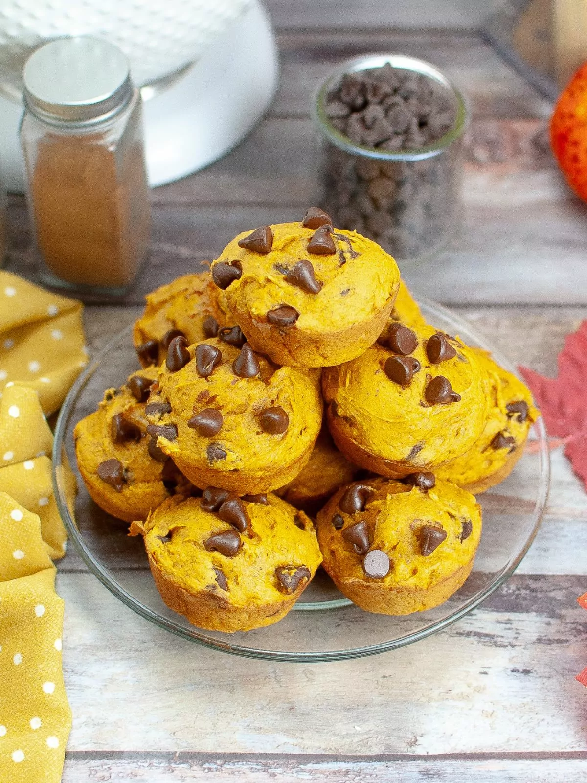 Pumpkin Chocolate Chip Muffins piled up on a plate with jars of chocolate chips and seasonings in the background