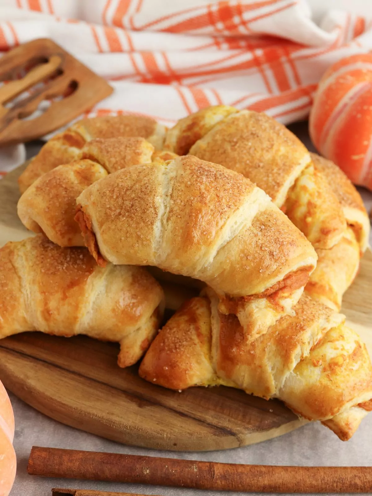 Pumpkin Cream Cheese Crescents on a wood board with an orange and white plaid towel in the background