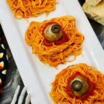 3 mounds of spaghetti on white platter with meatballs decorated like eyeballs for Halloween.