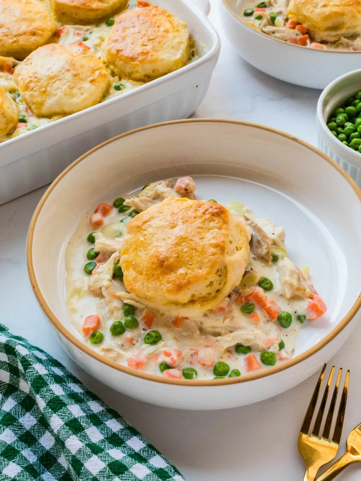 Chicken pot pie topped with biscuit served in a low white bowl. Casserole in the background